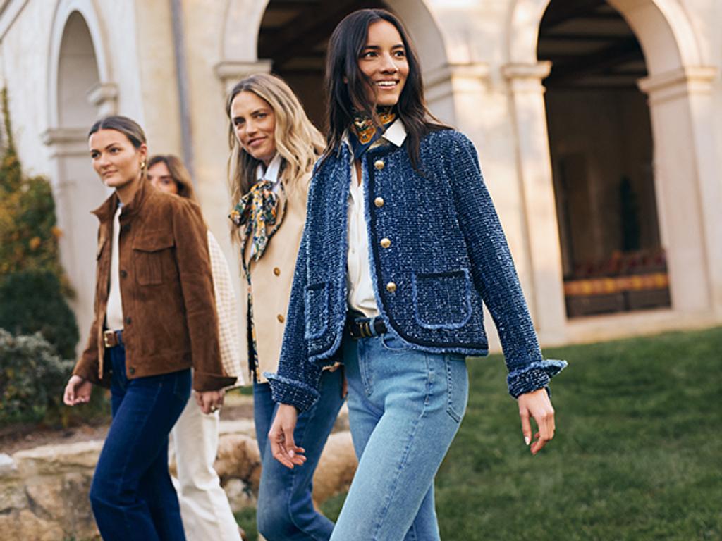 Three female models in various outfits walking across a green lawn