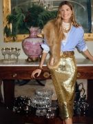 woman standing in living room wearing gold sequin skirt, blue button down shirt and fur stole