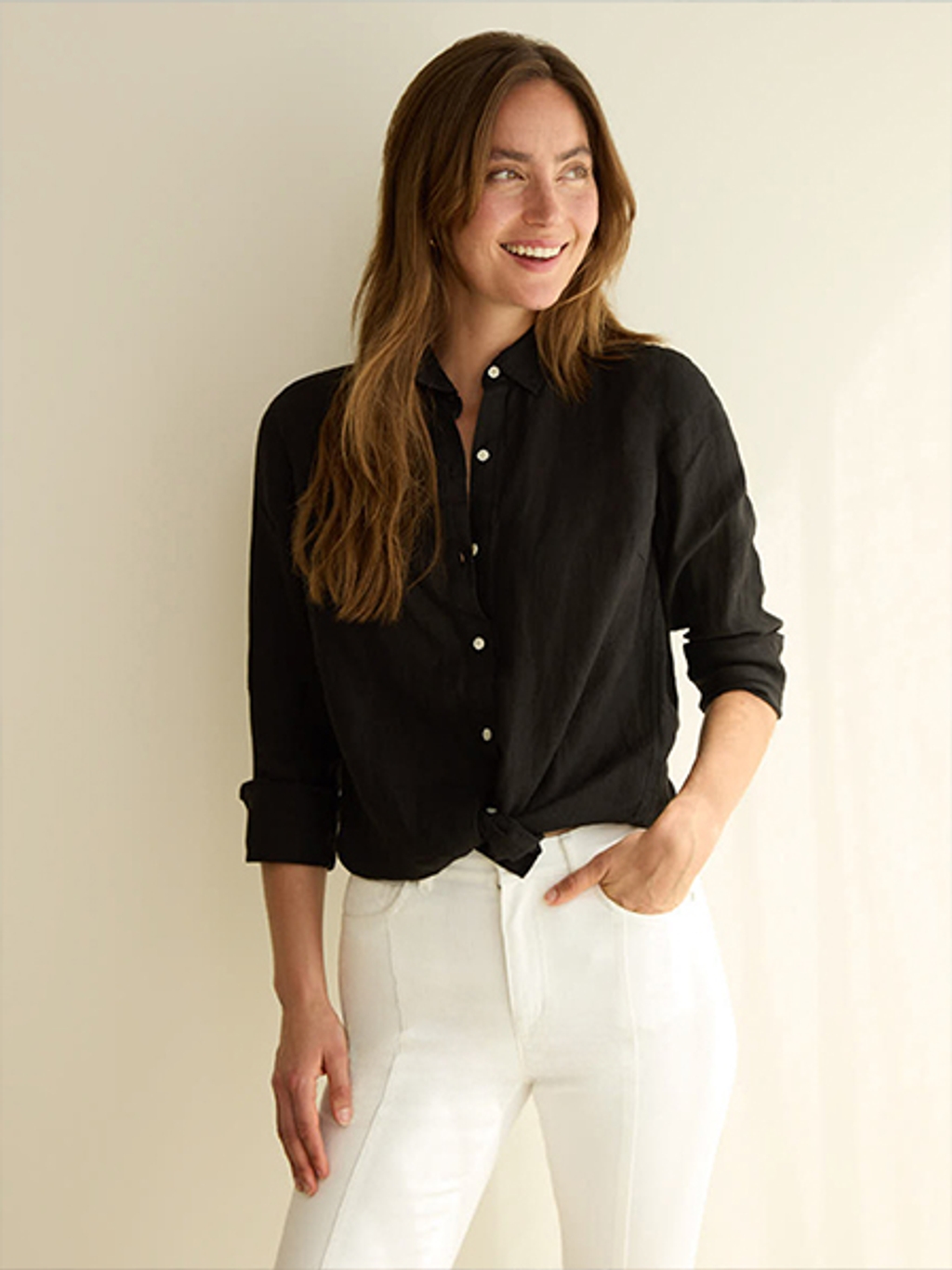 Woman smiling and wearing a black linen button up shirt and white denim jeans.