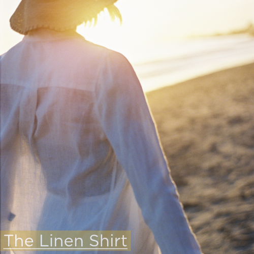woman on a beach at sunset wearing white linen shirt and straw hat
