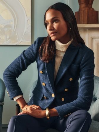 woman seated inside in living room wearing navy boucle double breasted blazer over off white ribbed turtleneck