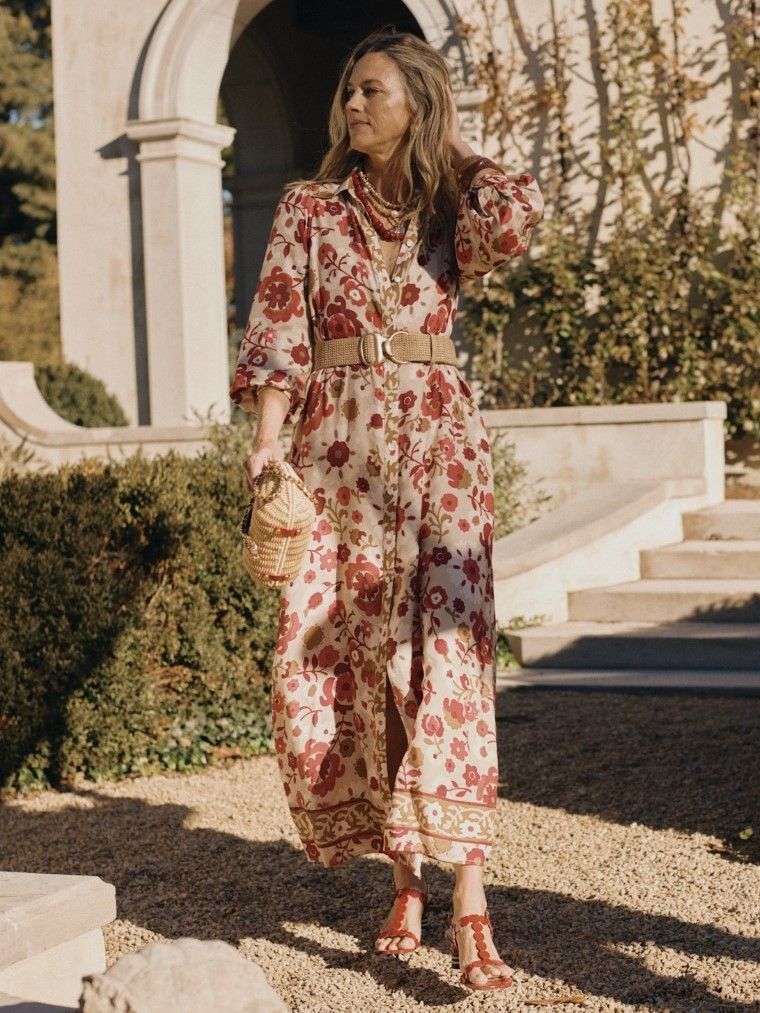 woman standing outside in red floral printed long dress with straw belt and wicker bag
