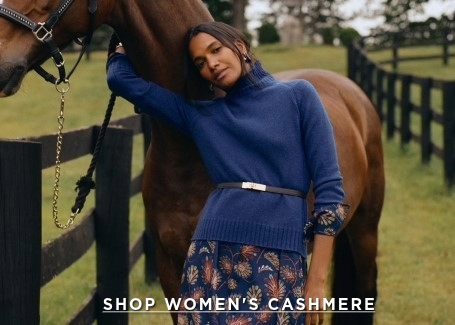 woman in field, leaning against horse, wearing navy cashmere turtleneck layered over navy floral printed dress