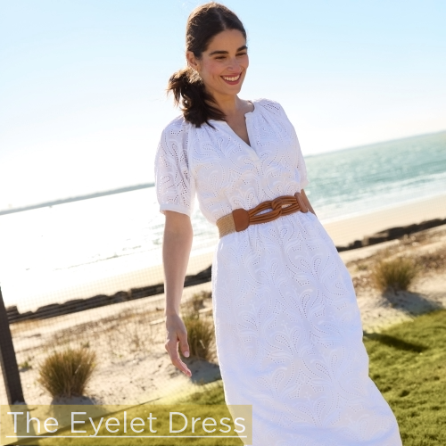 woman in white eyelet dress standing on lawn with beach in background