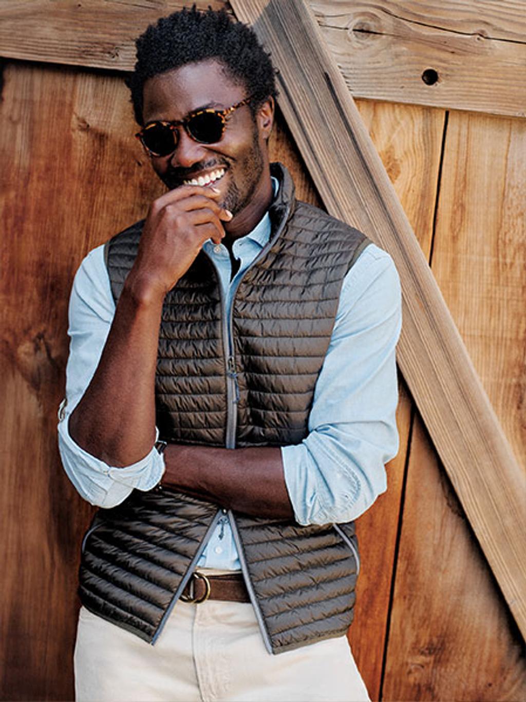 Male model wearing sunglasses and a blue long sleeve with a black puffer vest.