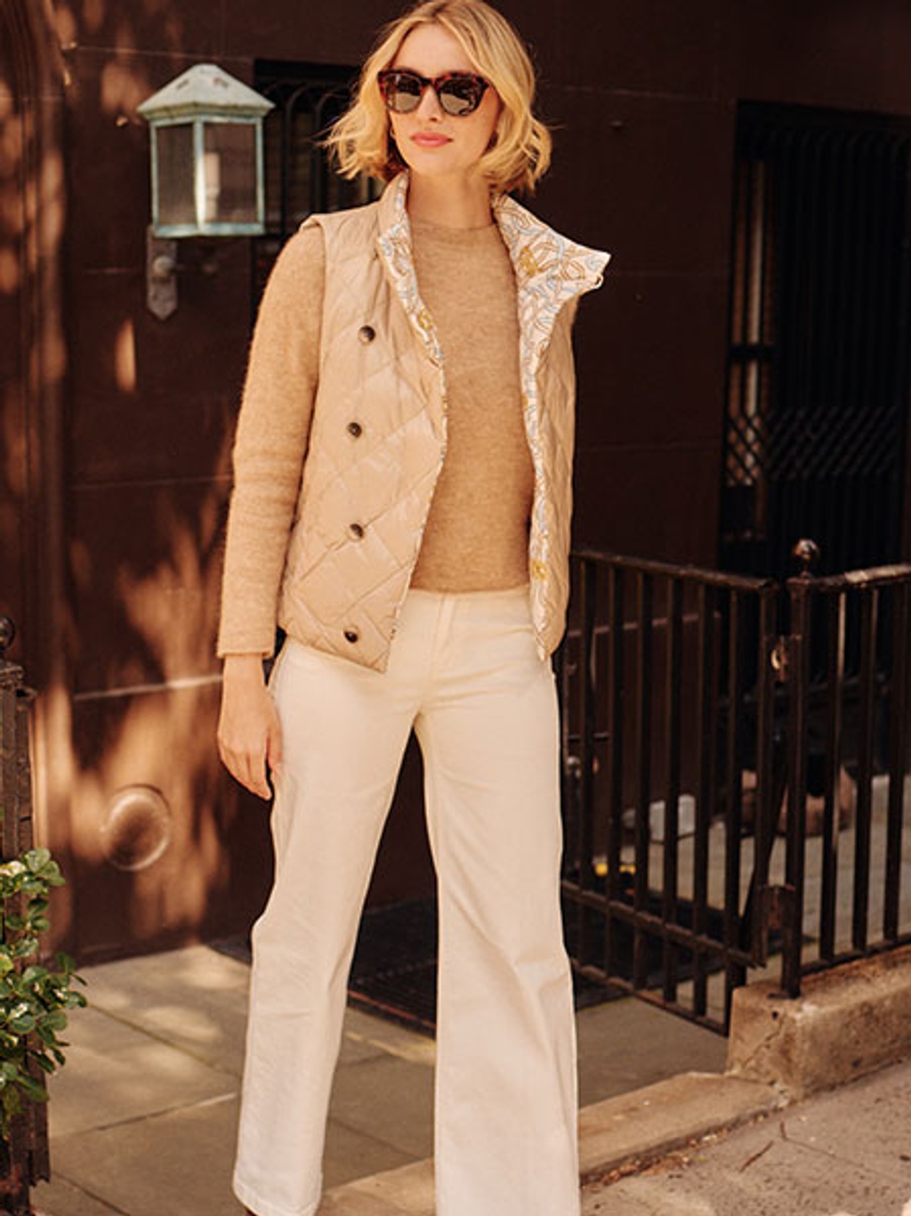 Model wearing a brown crewneck sweater, beige vest, and white pants 