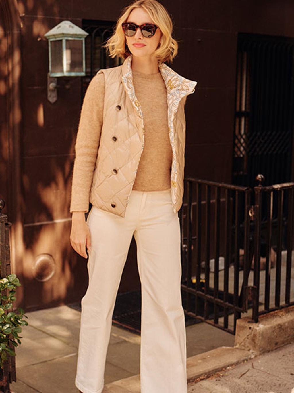 Model wearing a brown crewneck sweater, beige vest, and white pants 