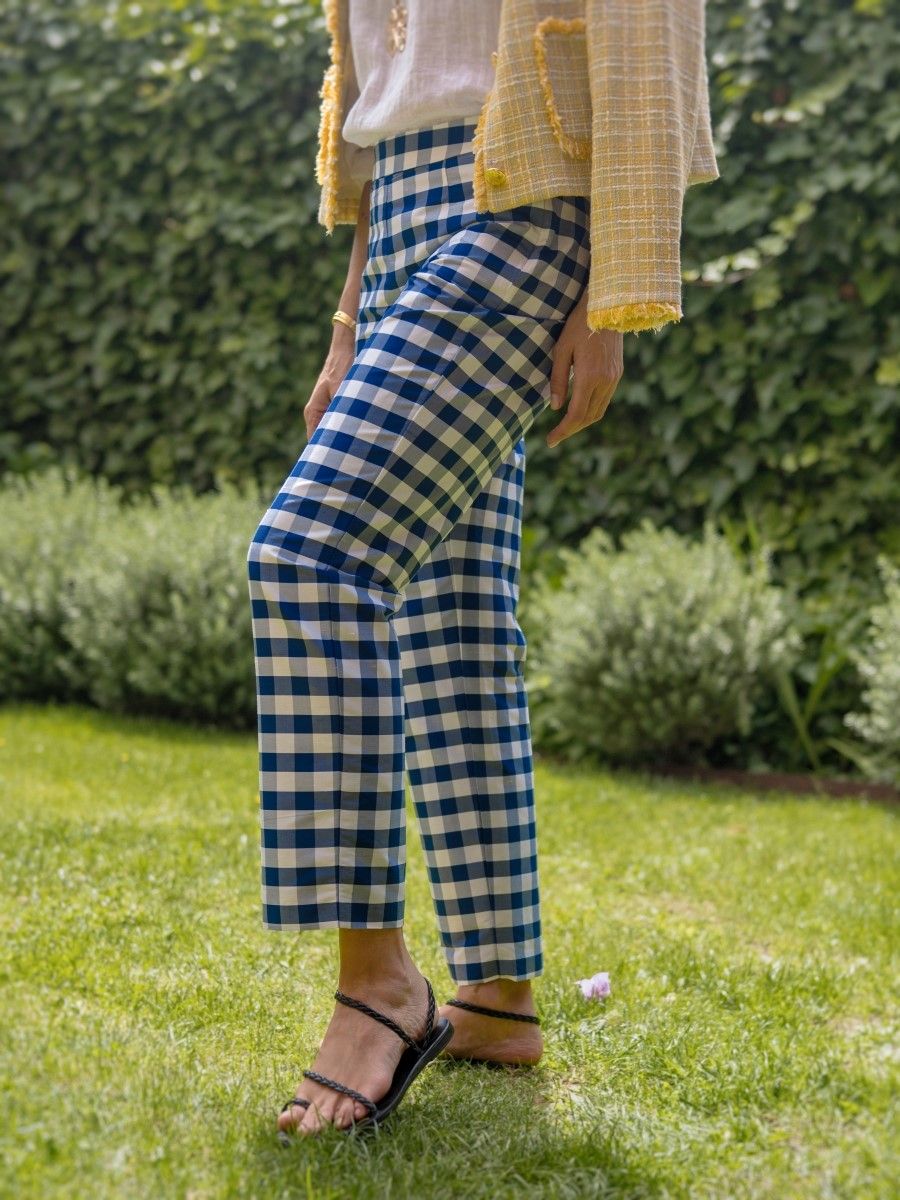 A person wearing blue and white gingham pants, a yellow jacket, and black sandals stands on green grass.