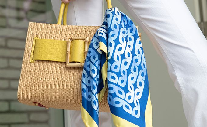Yellow leather and raffia handbag with blue and yellow scarf tied around handle
