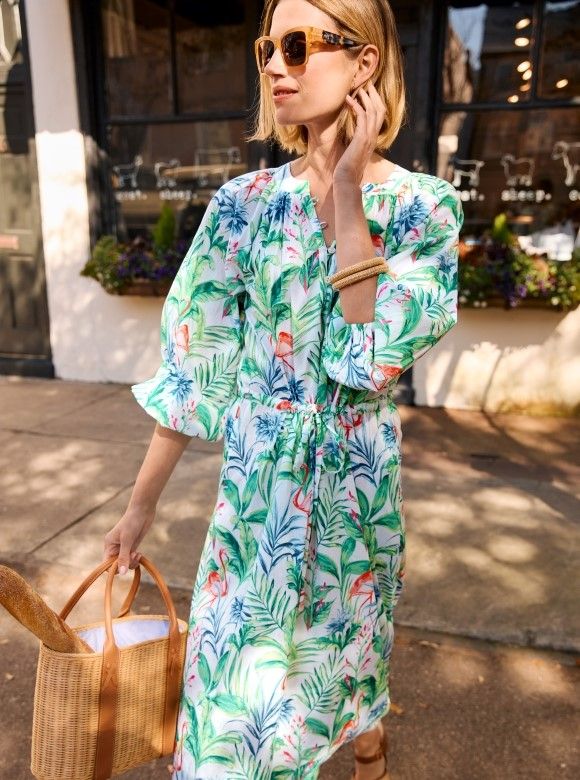 woman standing outside on the street wearing a white flowy blouson sleeve dress with drawstring waist and featuring a multi color botanical print