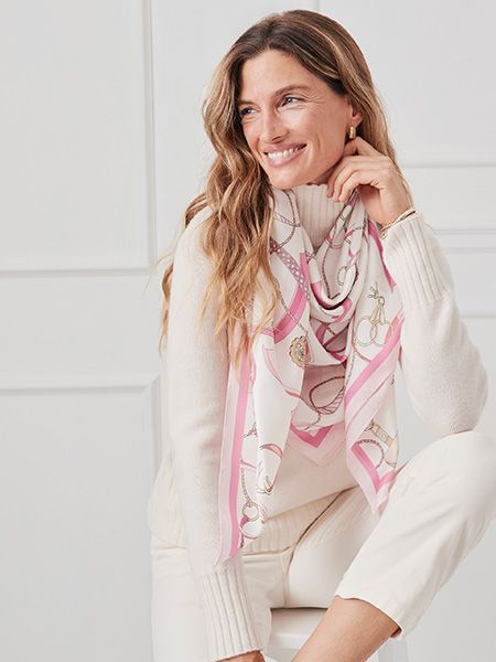 Woman in white shirt and pants with a pink and white chain-print scarf draped over her shoulders