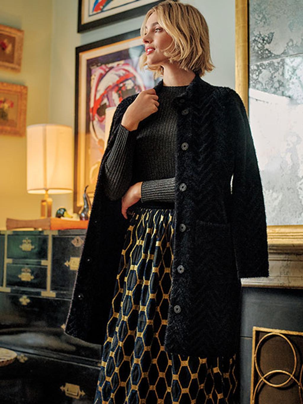 Model wearing sweater coat, turtleneck, and jacquard skirt in front of fireplace Model wearing sweater coat, turtleneck, and jacquard skirt in front of fireplace