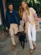 woman walking with dog and man outside wearing white jeans gold puffer and striped shirt