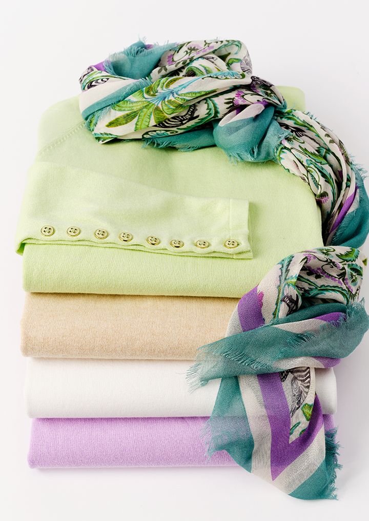 A woman in a coral pink tweed blazer smiles while leaning on a wooden bar.