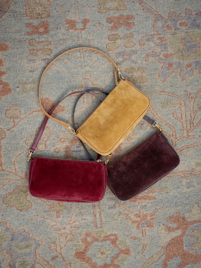 three womens suede shoulder bags laying on geo pattern carpet