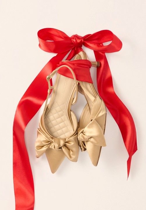 womens gold satin bow front slingbacks with red bow tied around them