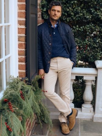 man standing outside on a terrace in khaki chino pants, navy sweater and navy quilted jacket