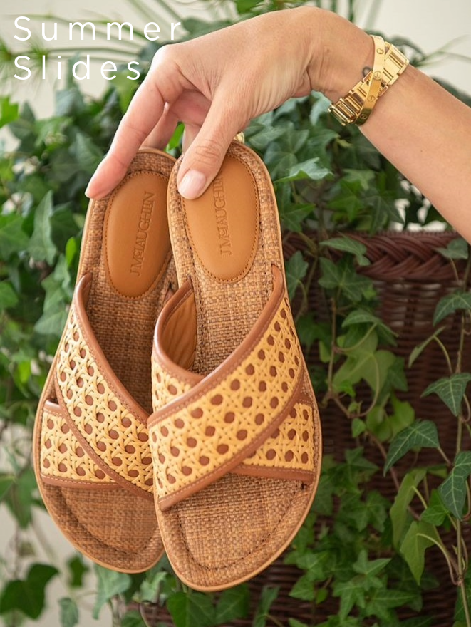 woman holding up a pair of rattan and leather sandals