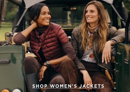 two women seated on the trunk of a jeep wearing quilted jackets