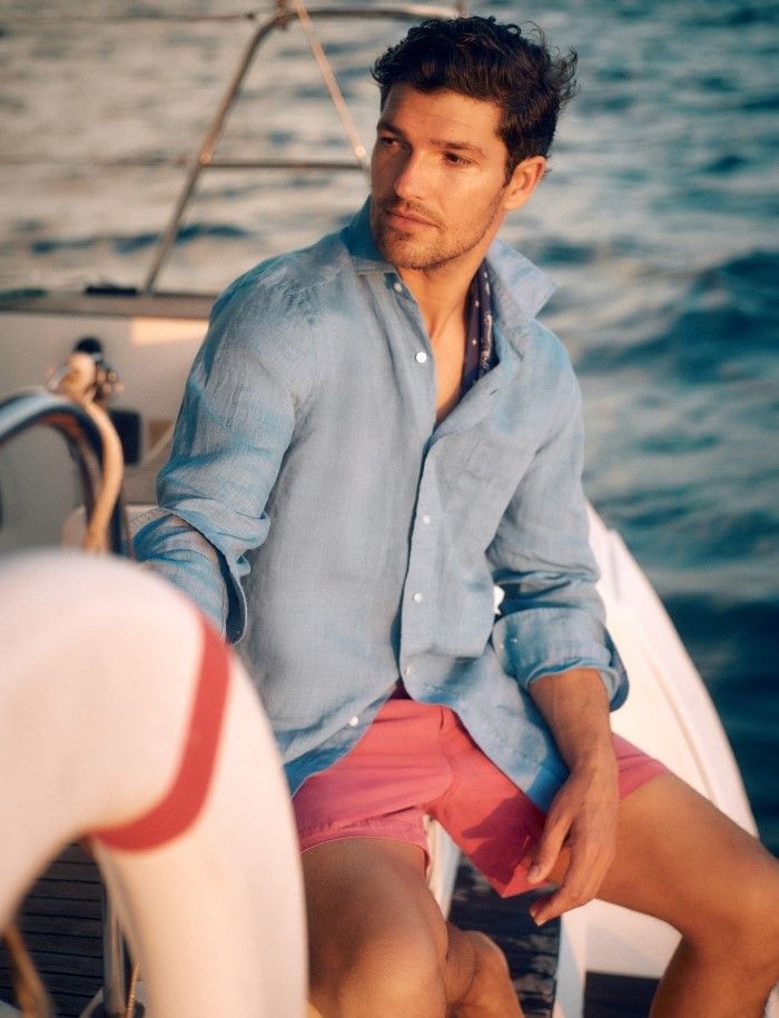 man seated on a boat wearing a chambray button down shirt