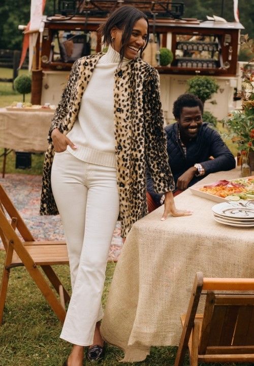 woman standing outside at a table wearing leopard faux fur coat, off white jeans and off white turtleneck