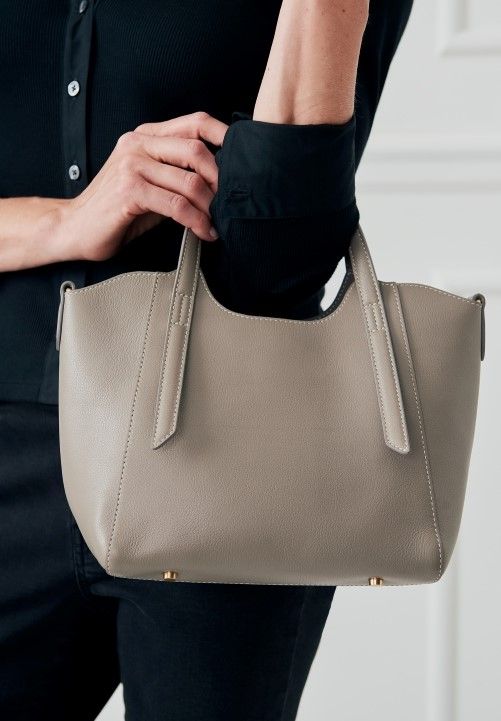 cropped image of woman holding gray leather small tote bag standing in front of white studio backdrop
