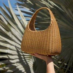 natural wicker top handle bag lifted in air with palm leaves in background