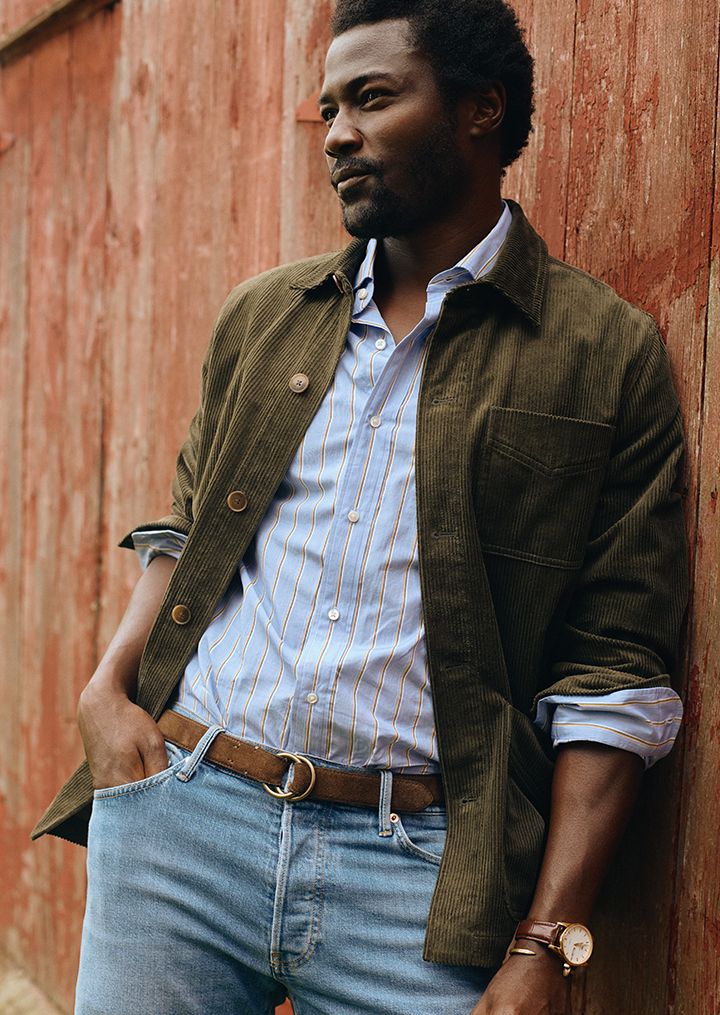 man leaning against barn in olive corduroy jacket and jeans