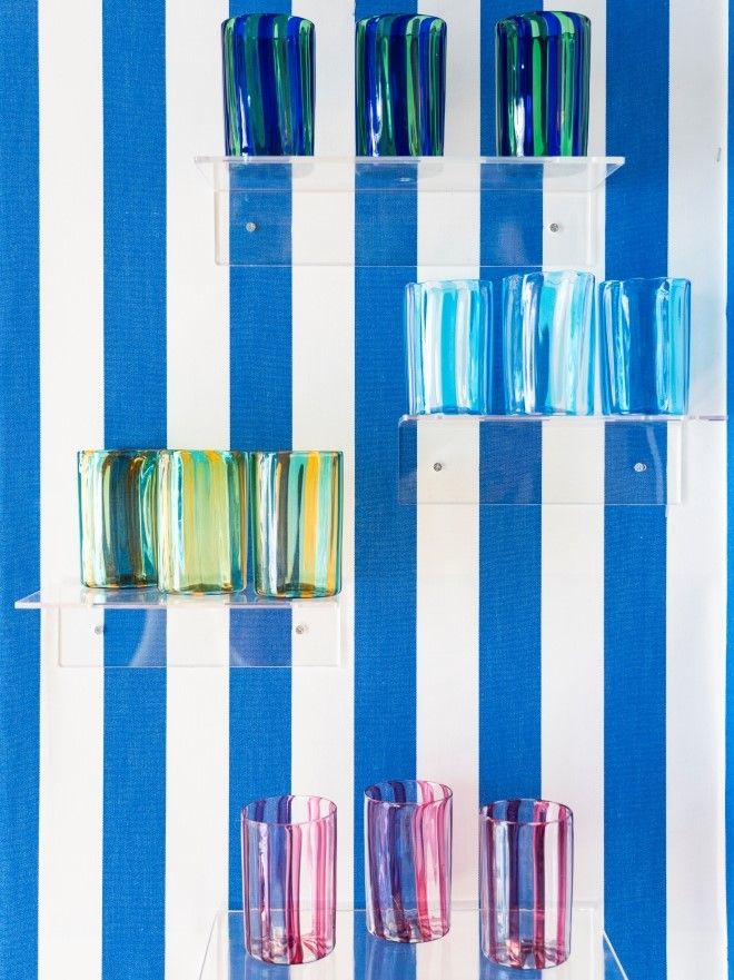 blue and white striped wall with four shelves and different murano glassware on each shelf