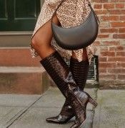 cropped image of woman wearing tall croc embossed dark brown leather boots and holding a dark brown leather crescent shaped bag