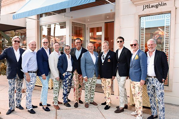 Ten men in blazers and patterned tropical trousers pose in front of a J.McLaughlin store.
