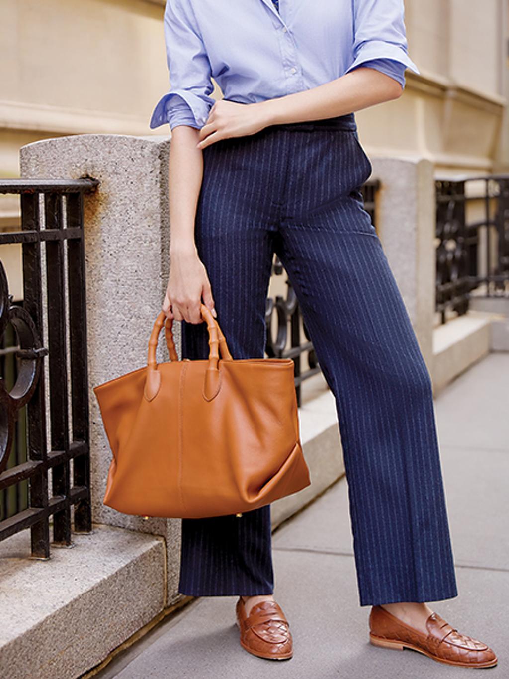 Women on the street wearing blue pants, a blue button-down shirt, and brown loafers holding a brown handbag.