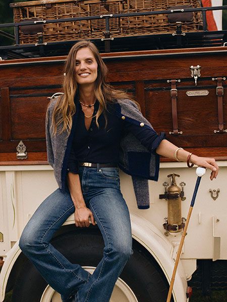 Female model wearing navy top, blue jeans posing on a white vehicle.