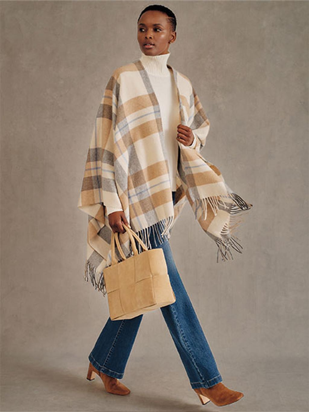 Model wearing white turtleneck with plaid wrap, jeans, woven bag, and boots.