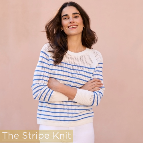 woman standing in front of light mauve wall wearing white crewneck knit sweater with blue stripe