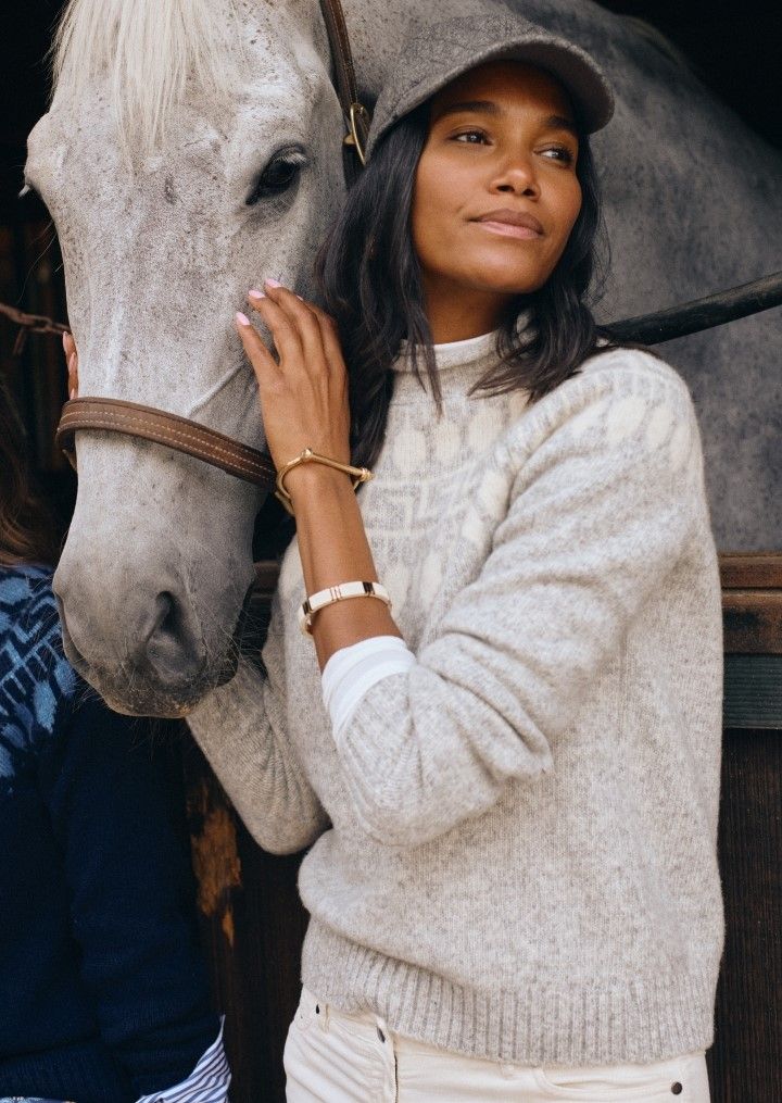 woman in light gray fair isle roll neck sweater nuzzling horze in stable