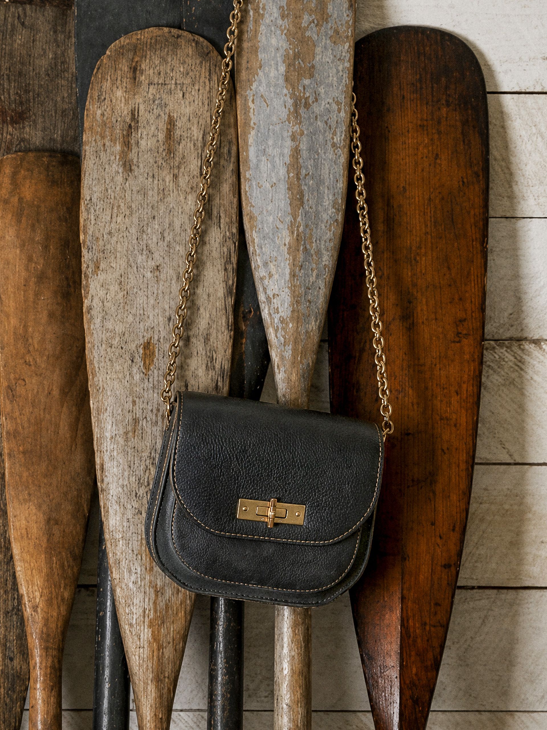 Black leather purse with a gold chain strap hanging in front of rustic wooden paddles.