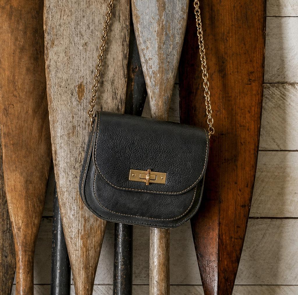 Black leather purse with a gold chain strap hanging in front of rustic wooden paddles.
