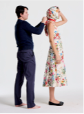A man helps a woman in a floral dress tie her headscarf.