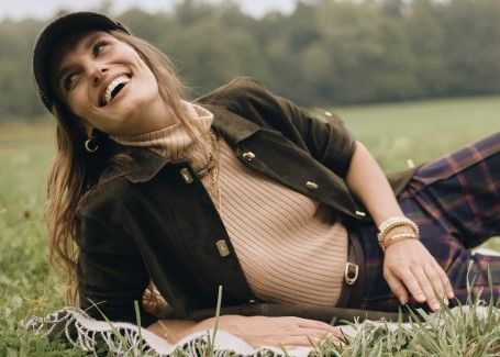 woman laying on the grass outside wearing camel ribbed turtleneck and baseball hat