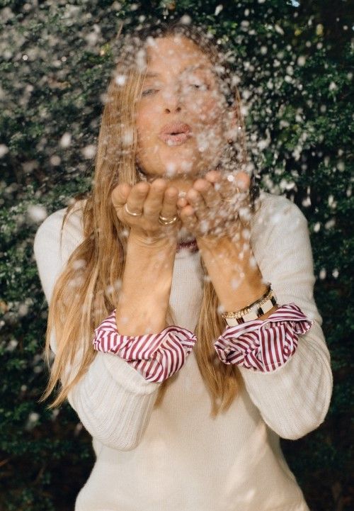 woman in off white cashmere turtleneck blowing snow in the air outside