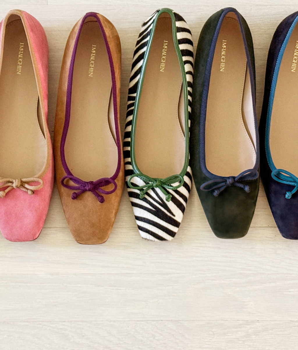 A row of five ballet flats in pink, tan, zebra print, dark green, and dark blue, each with a contrasting trim and bow.