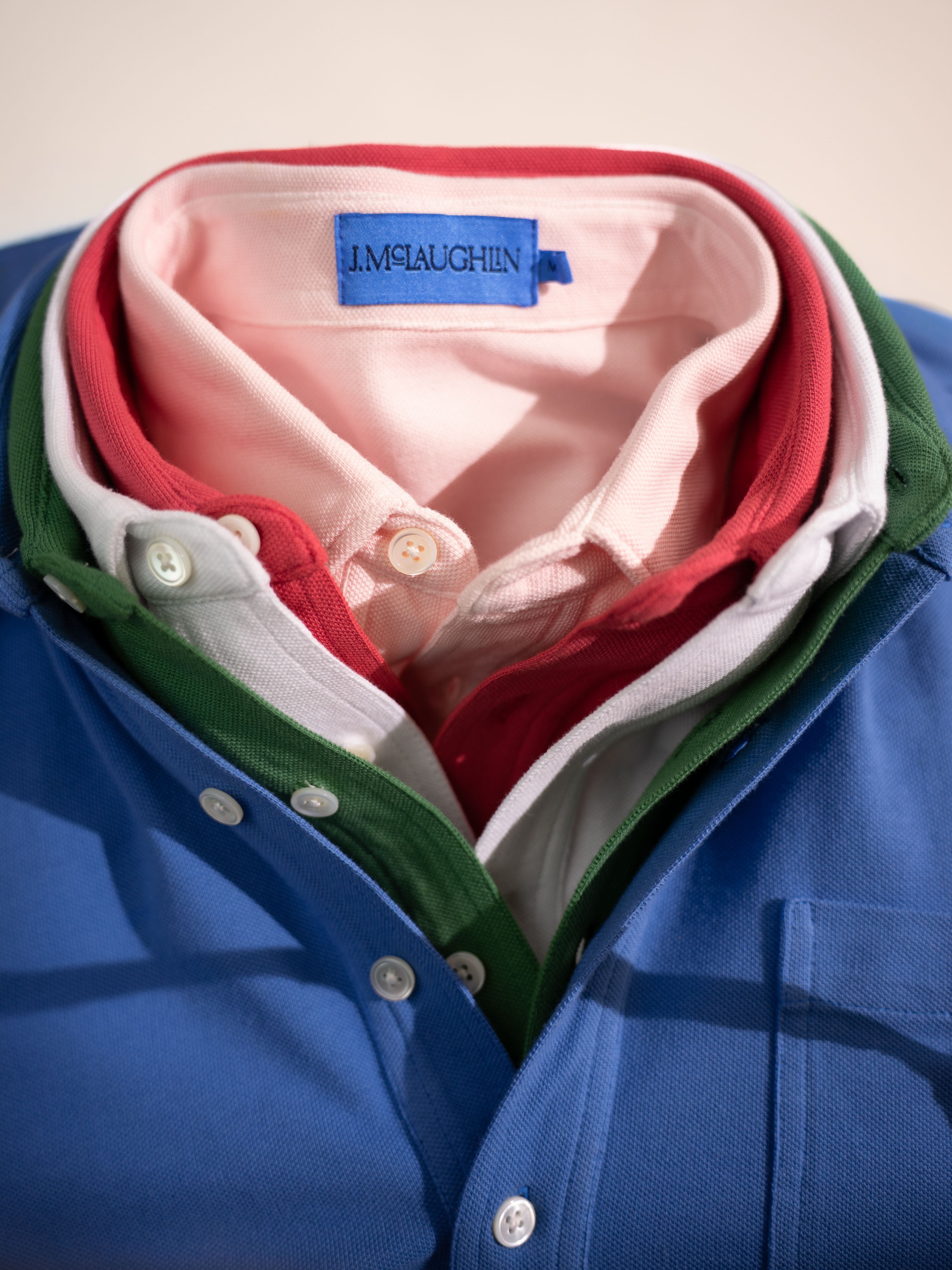 Five J.MCLAUGHLIN polo shirts stacked by color: pink, red, white, green, and blue.