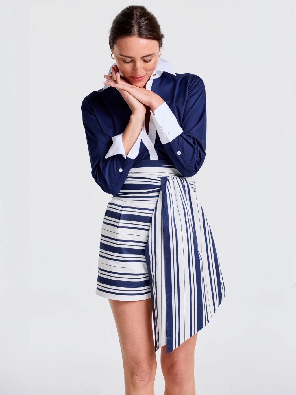 A woman in a navy collared shirt with white cuffs, and white and navy horizontally striped shorts with a vertically striped draped panel.