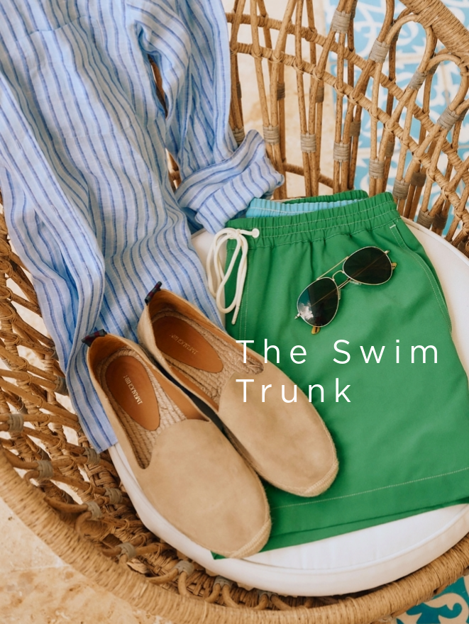 men's green swim trunks, tan suede espadrille and sunglasses positioned atop a rattan chair