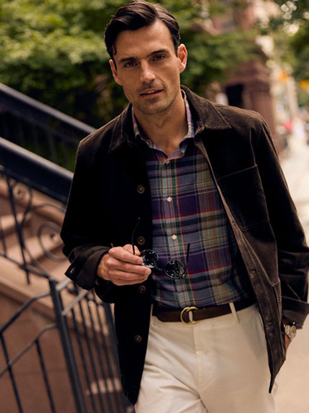 Male model wearing a brown jacket and plaid button up top with white pants.