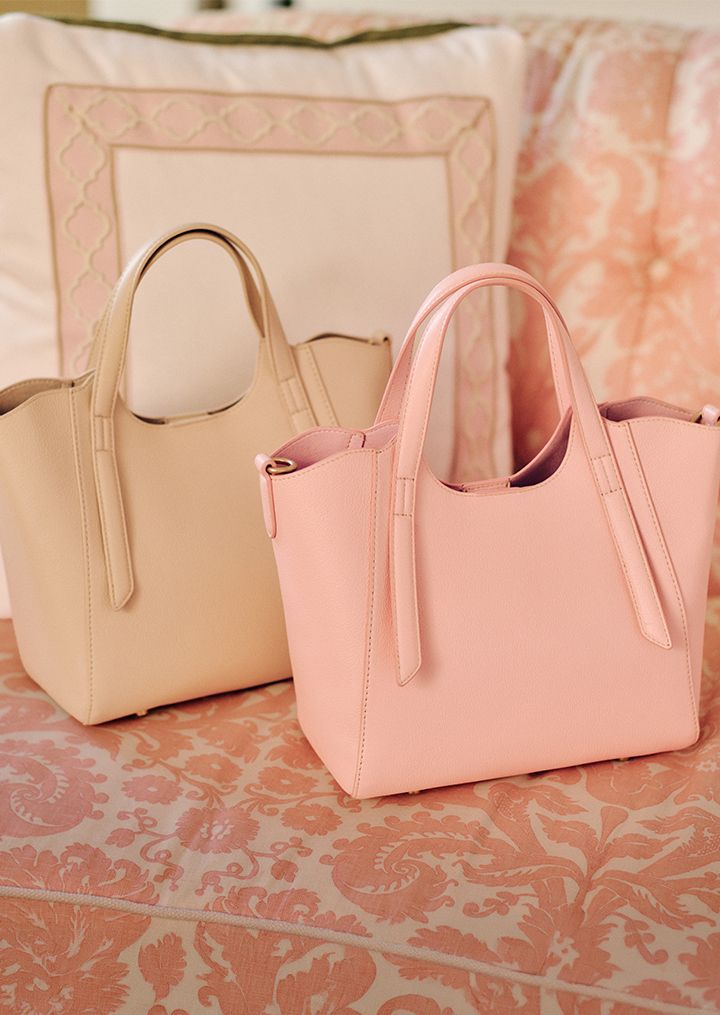 A person in a tied blue striped shirt and pink skirt holds a small straw bag with pink trim.