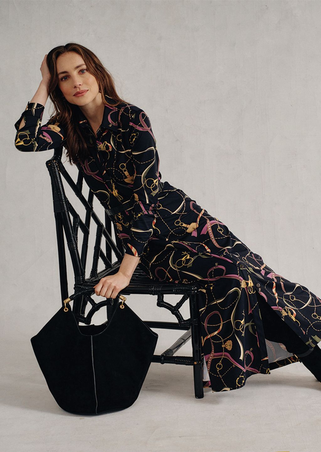 Woman in seated in a maxi-length black heraldic print dress.