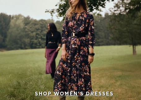woman standing in a field wearing a long black floral printed dress with black belt