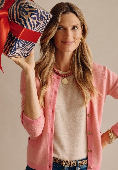 woman wearing pink cashmere cardigan and holding zebra wrapped gift box with red bow